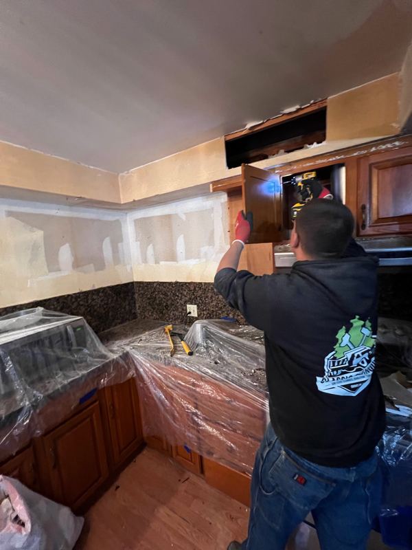 Crew member removing kitchen cabinets with counters and appliances covered in plastic during a light demolition job by Classic Cleanouts